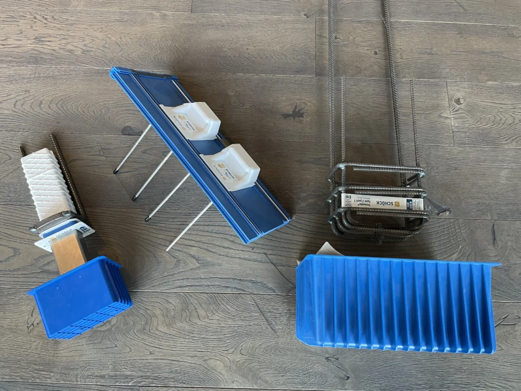 Die Bauteile Schöck Tronsole® Typ T, Z und Q liegen nebeneinander auf einem braunen Holzboden